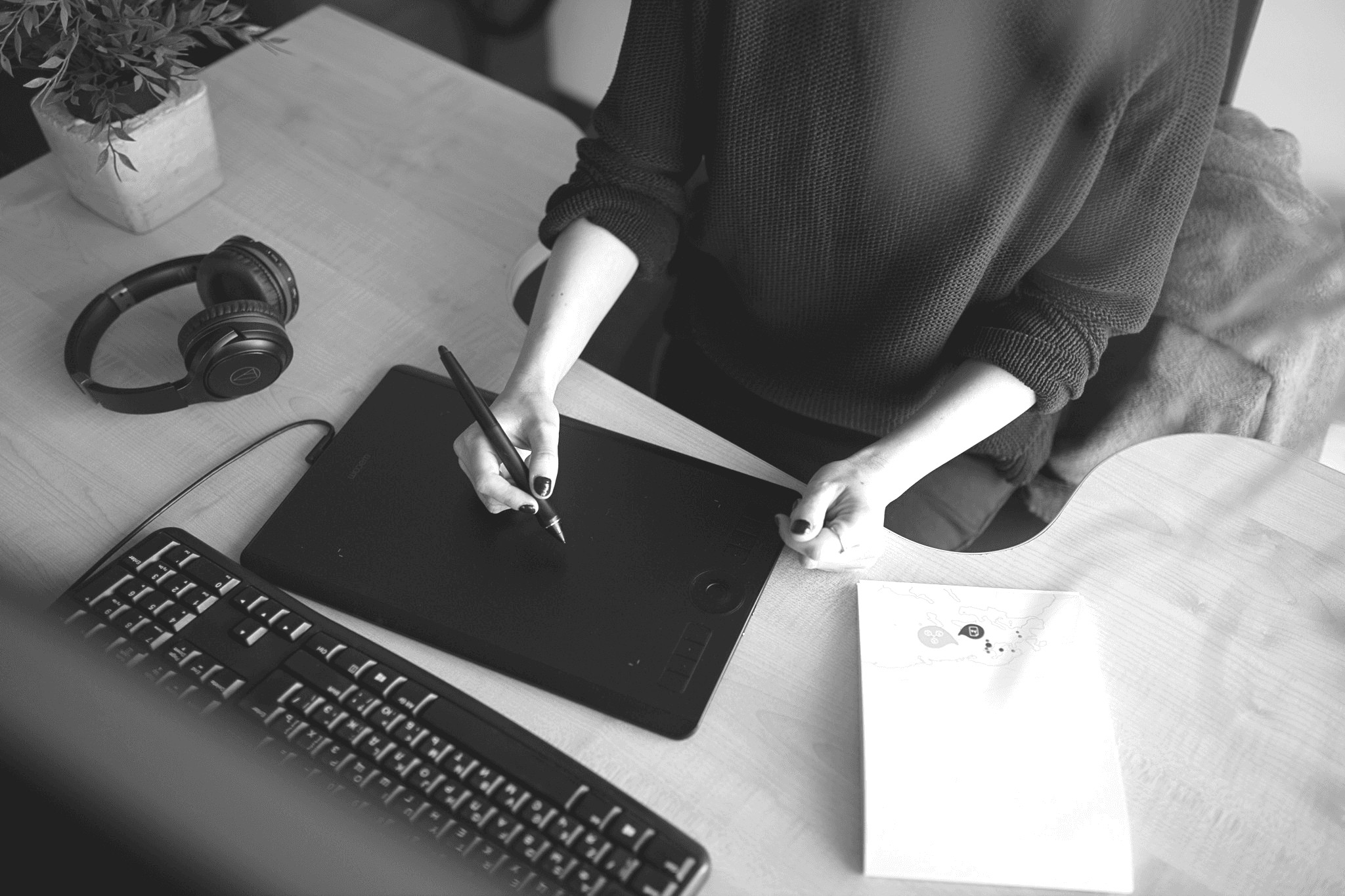 A person in a black shirt uses a laptop and a tablet, surrounded by a mouse and a notebook on a desk.