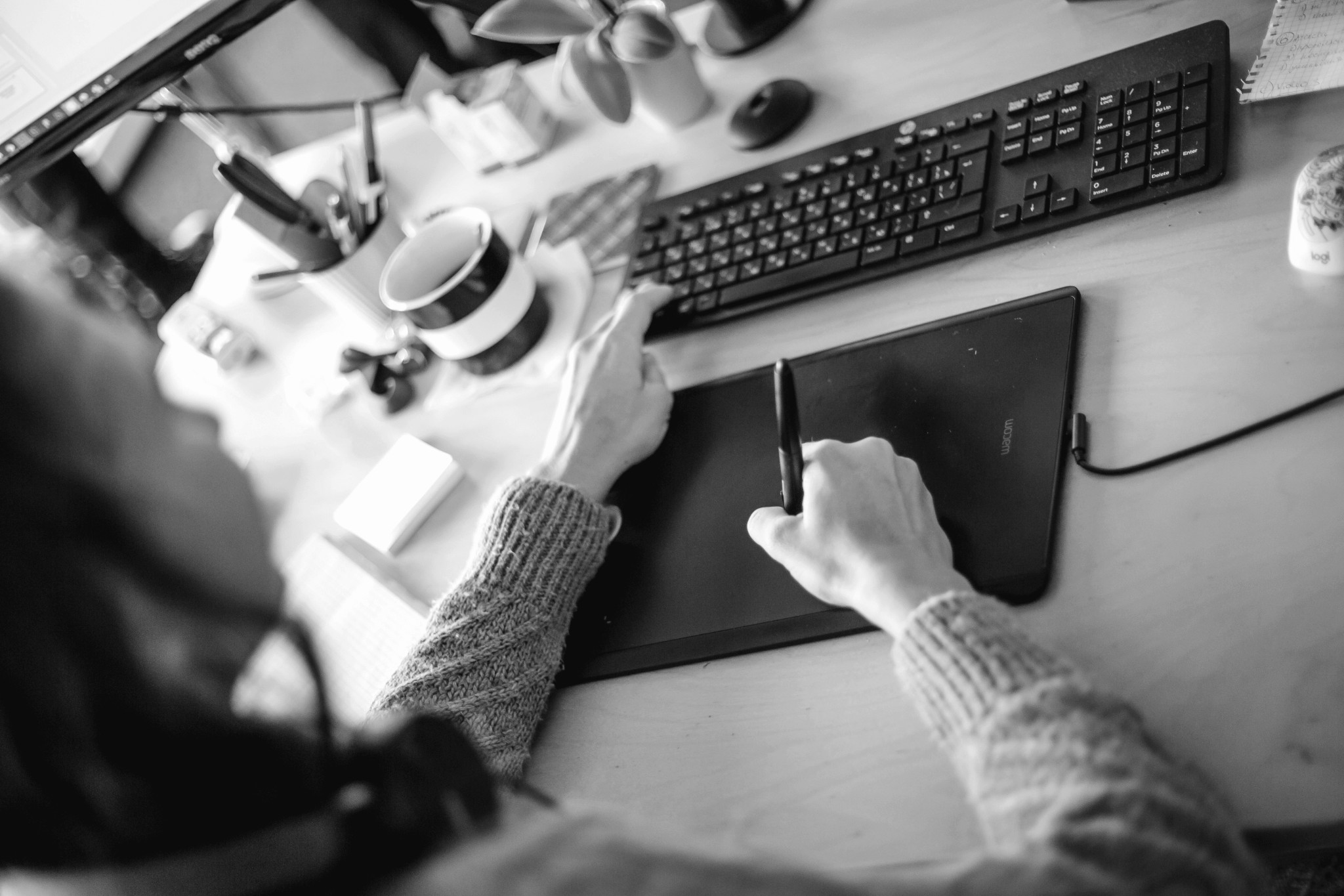 A close-up of a person's hand using a mouse on a desk, with a cluttered workspace in the background.
